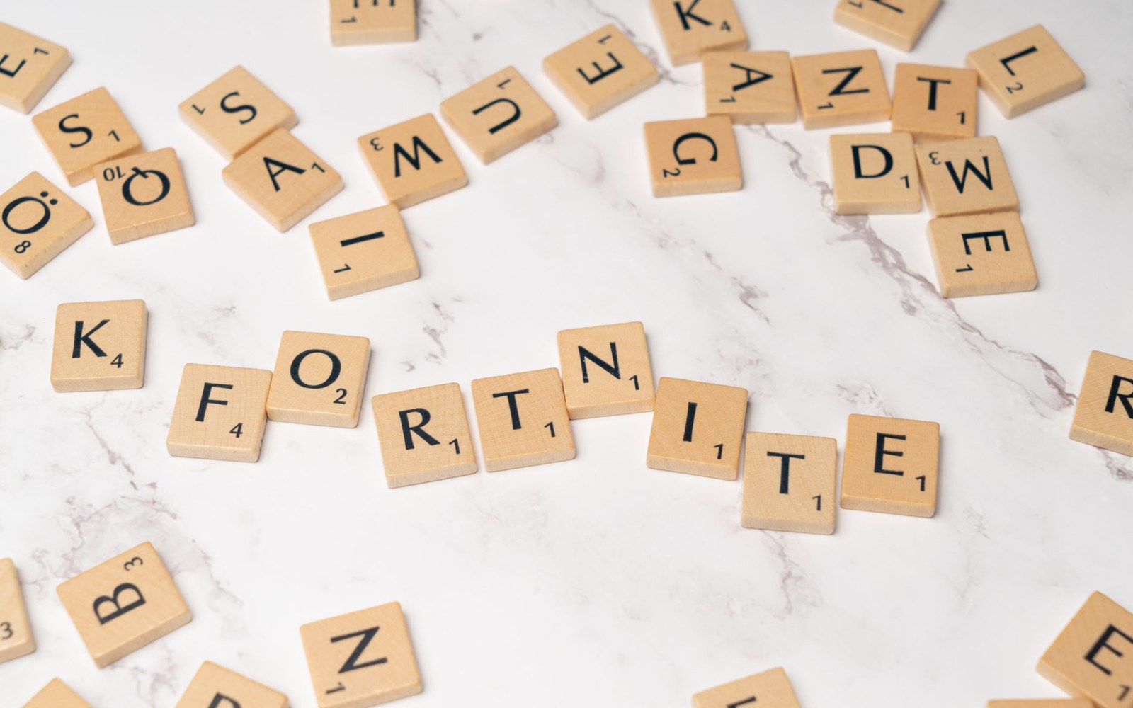 Scrabble tiles spelling "Fortnite" scattered among other lettered tiles on marble