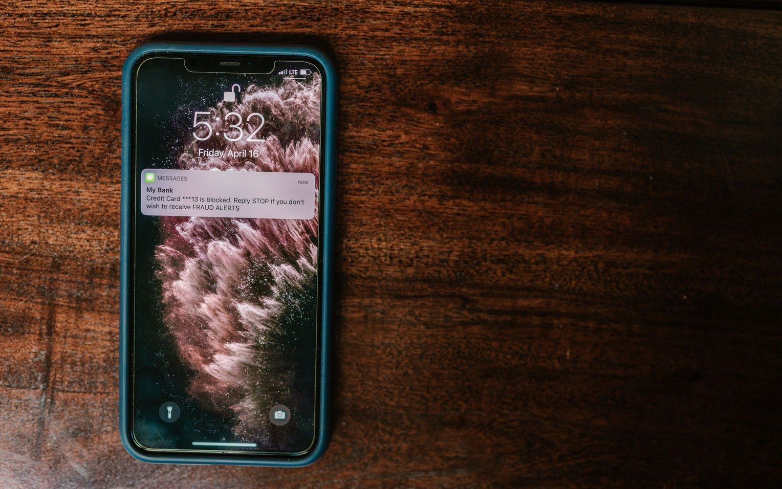 Smartphone lock screen showing a bank fraud alert text message about a blocked credit card