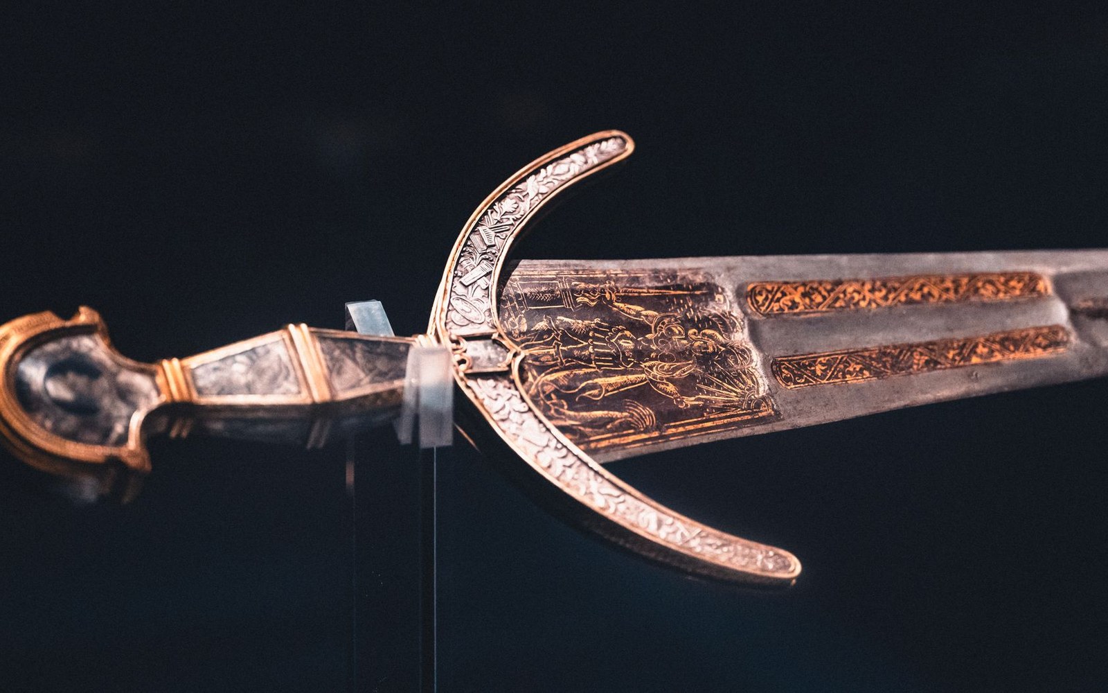 An ornate sword hilt with gold engravings displayed under museum lighting