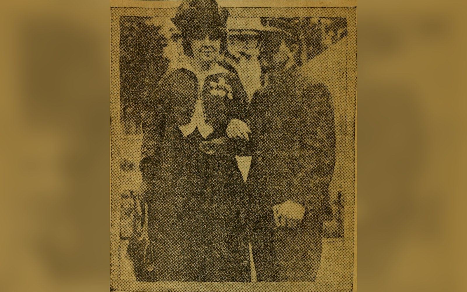 Faded newspaper clipping of a woman and man in early 1900s attire walking arm in arm
