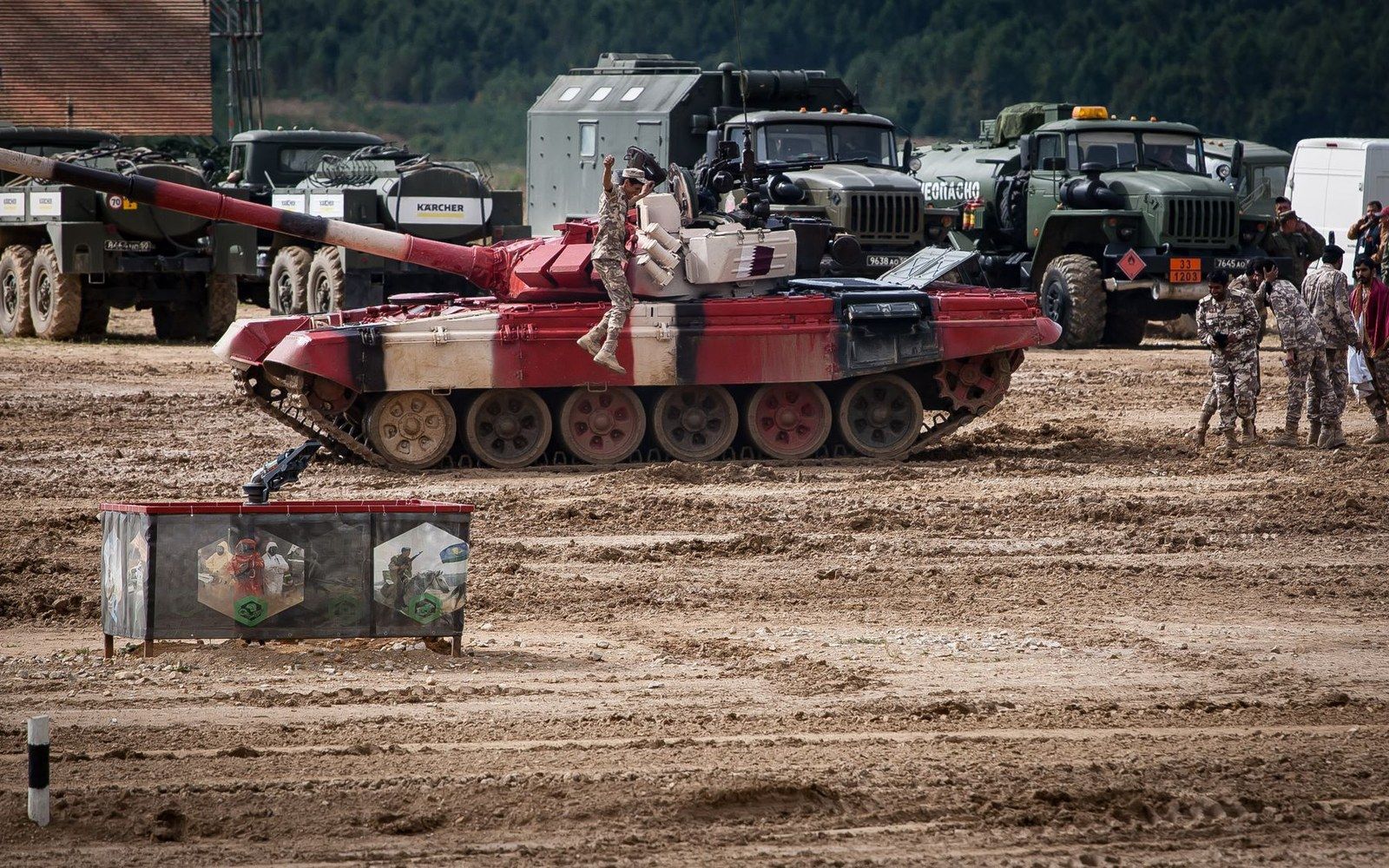 Soldier stands atop a red-painted tank as military trucks line up in the background