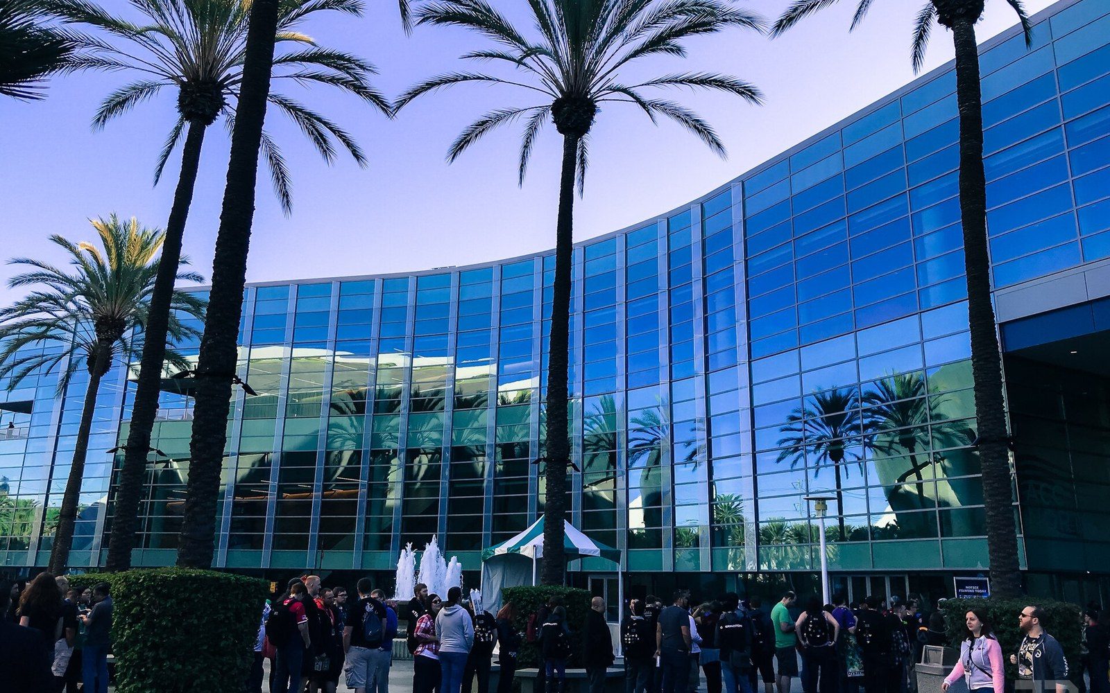 Crowds gather outside a glass convention center lined with tall palm trees