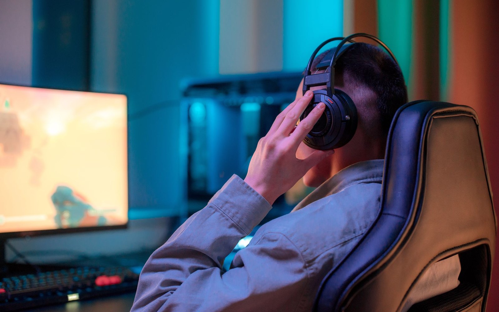 A gaming headset resting on a desk in front of a monitor displaying a WoW character-selection screen, room ambient light only