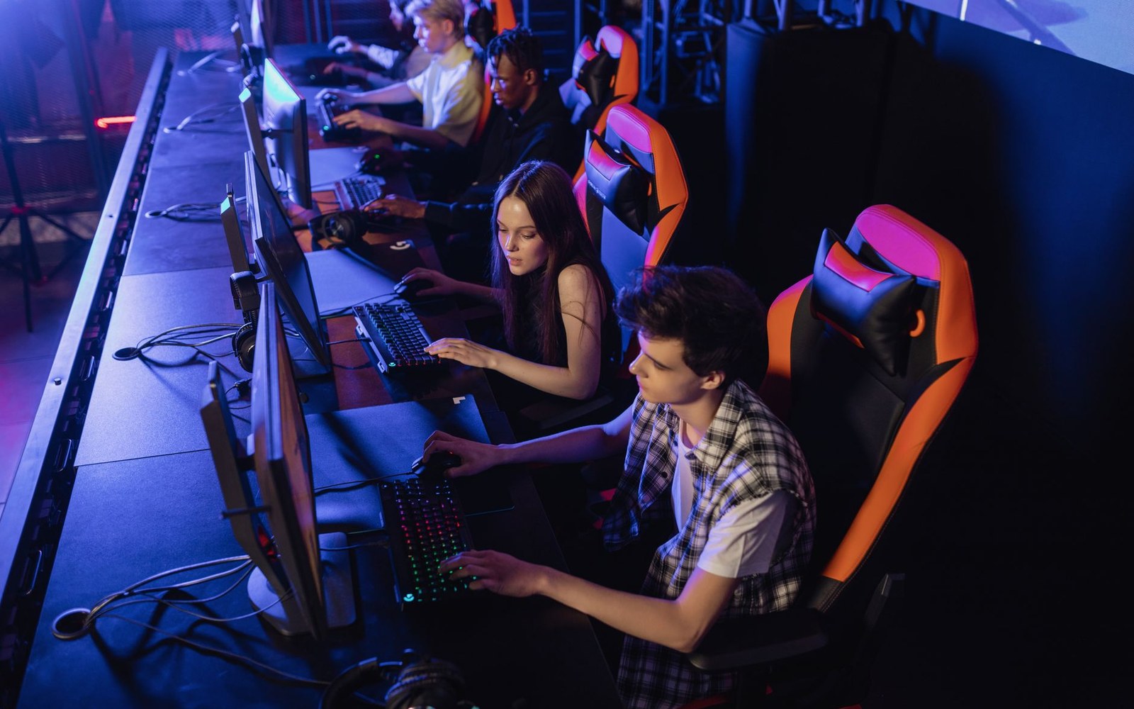 An overhead view of a LAN-party row — monitors, cables, adult players mid-session under low ambient light